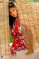 A woman in a red kimono leaning against a bamboo curtain.