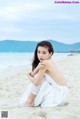 A woman in a white dress sitting on a beach.
