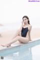 A woman in a black bathing suit sitting on the edge of a pool.