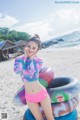 A woman in a bikini standing on a beach next to a tire.