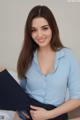 A woman in a blue shirt is sitting on a bed.