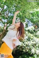 A woman in a white shirt and yellow skirt standing under a tree.