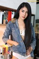 A woman in a denim jacket posing in front of a bookshelf.