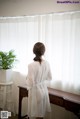 A woman standing in front of a window wearing a white robe.