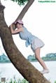 A woman leaning against a tree by the water.