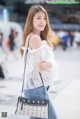 A woman in a white blouse and denim shorts holding a black and white bag.