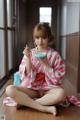 A woman in a pink and white kimono sitting on the floor eating a bowl of food.