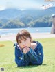 A young woman laying on the grass in front of a lake.