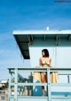 A woman in a bikini standing on a lifeguard tower.