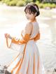 A woman in a white and orange dress standing by the water.