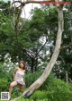 A woman sitting on a tree branch in the woods.